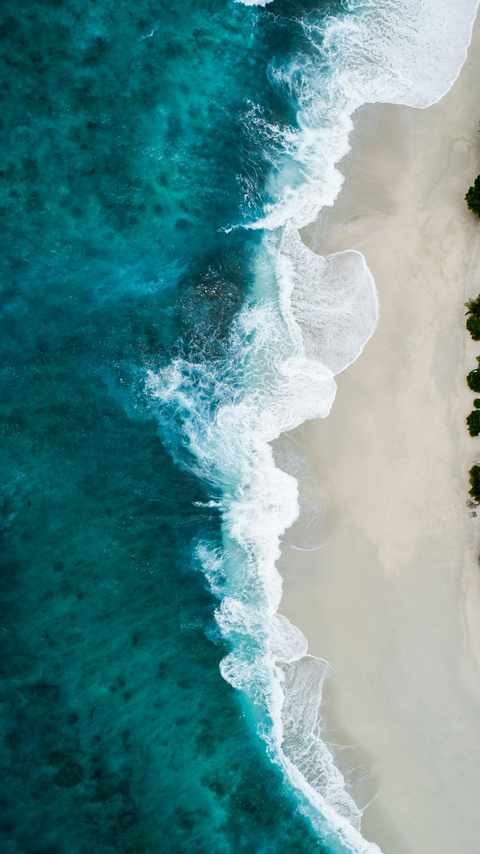 An aerial view of turquoise ocean waves meeting a pale sandy beach